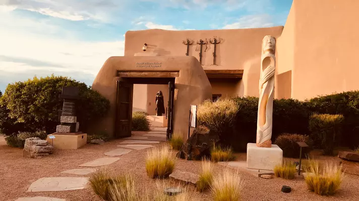 A sculpture in front of an adobe structure.