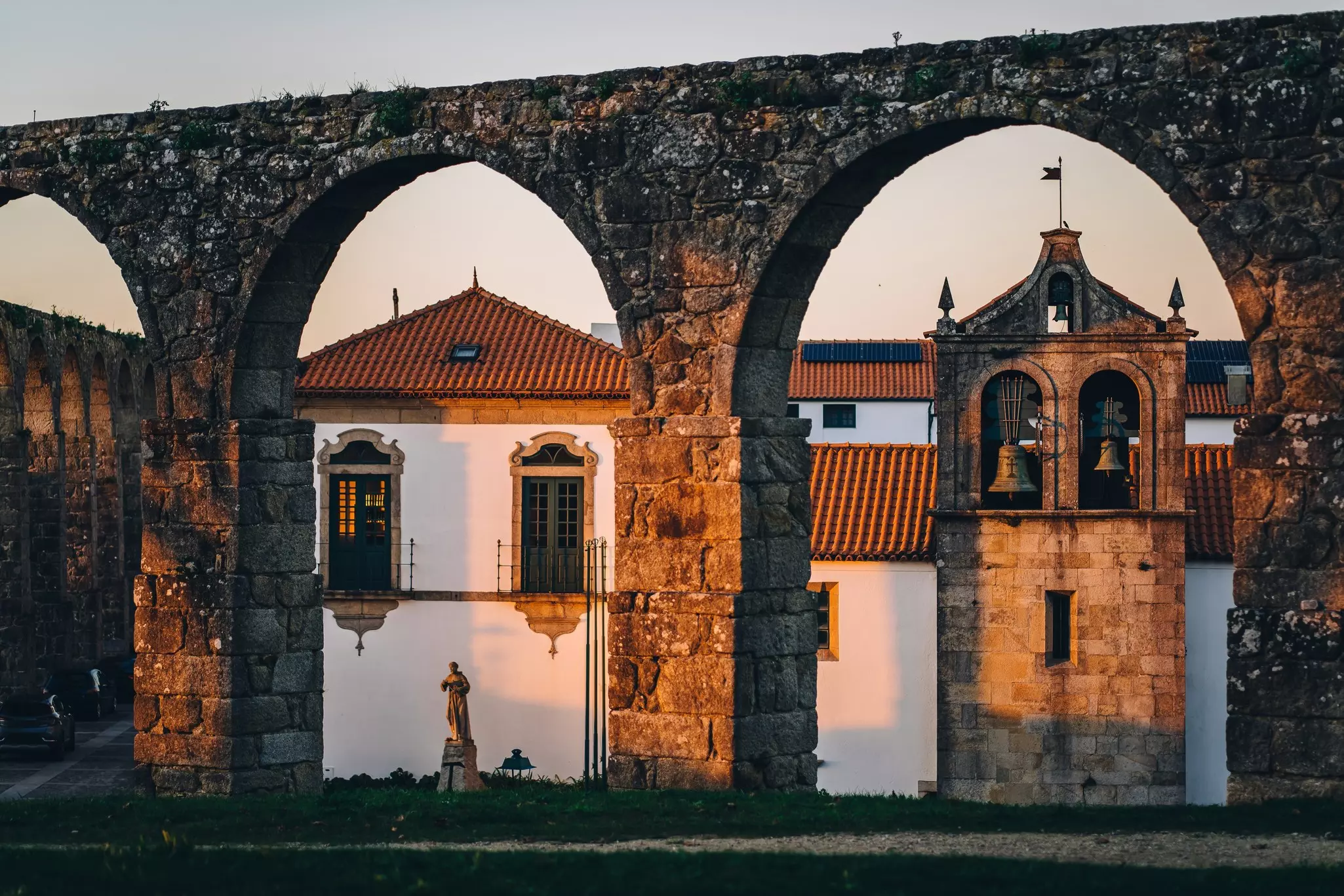 An old stone aqueduct with round arches is pictured at sunset in front historic buildings