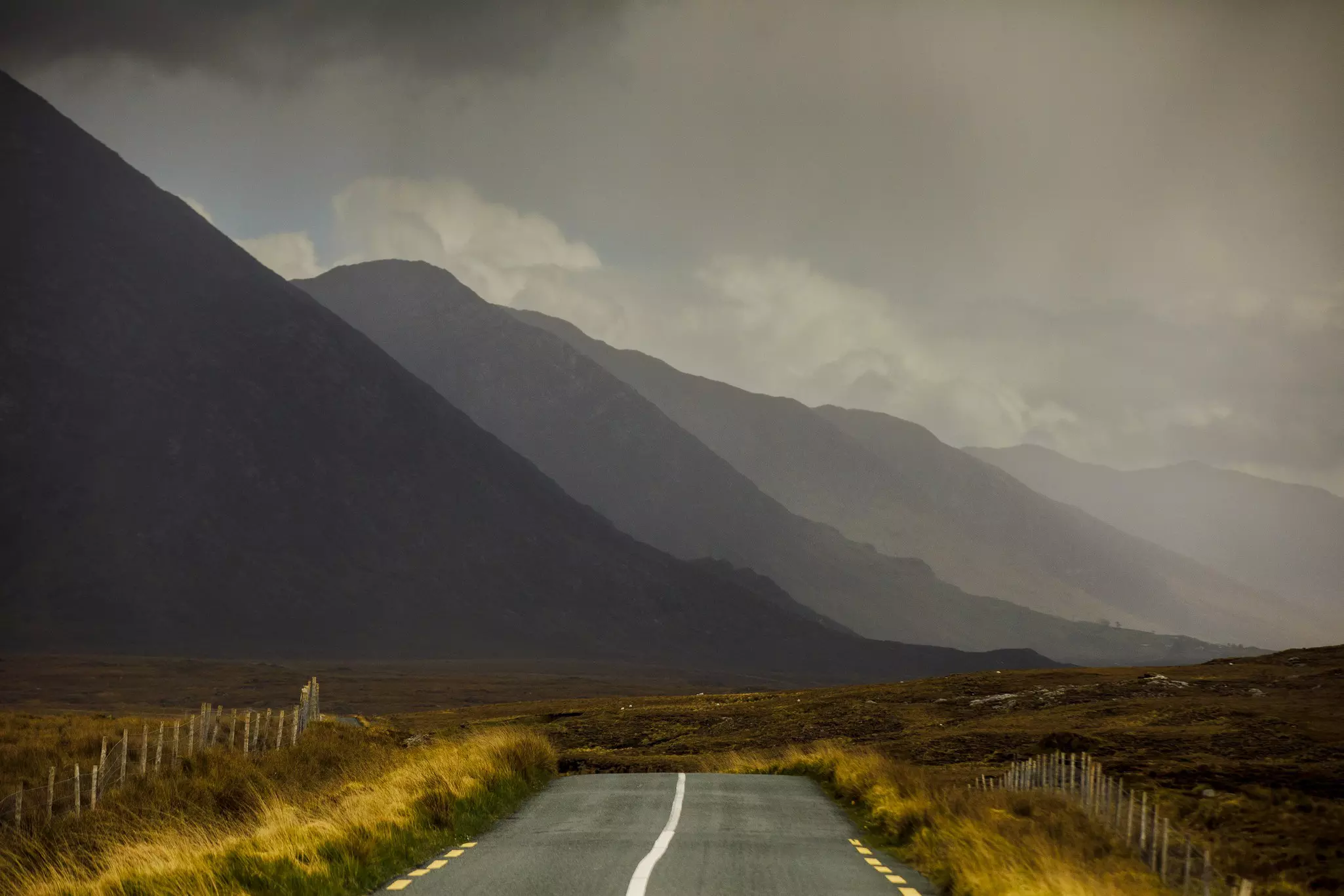 A road leads toward mountains in the distance, dramatically lit by mist and storm clouds.