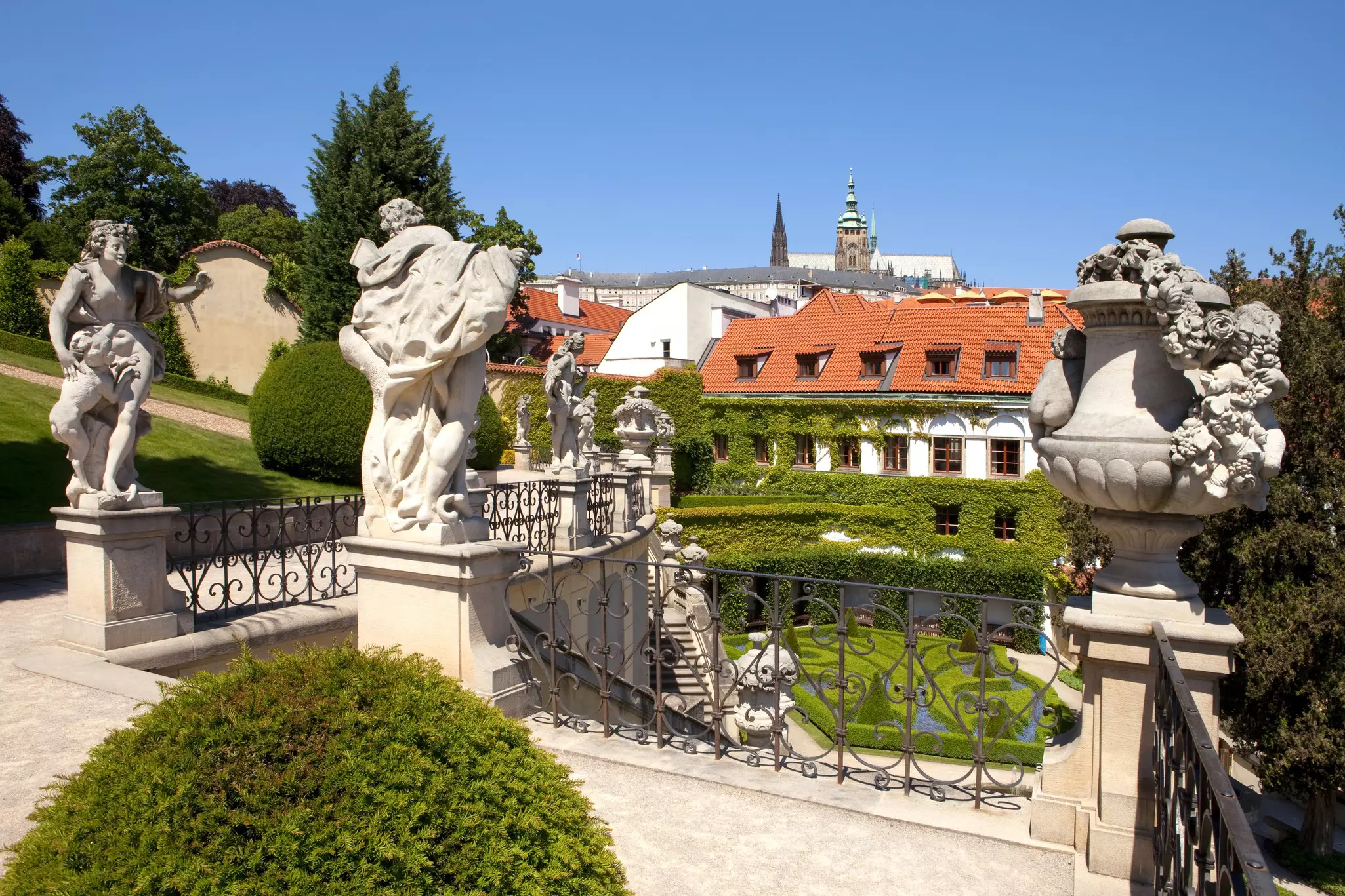 A staircase lined with statues leads down to a grassy area.
