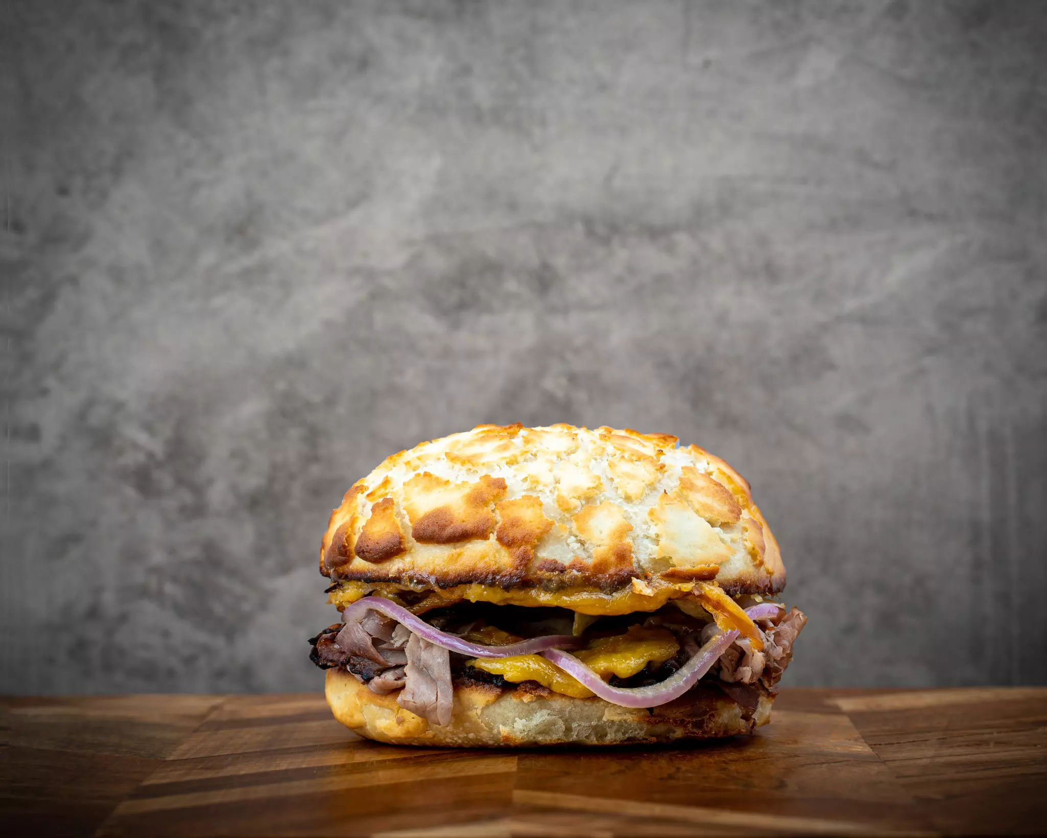 A sandwich made with roast beef and onions with a biscuit is displayed on a wooden table.