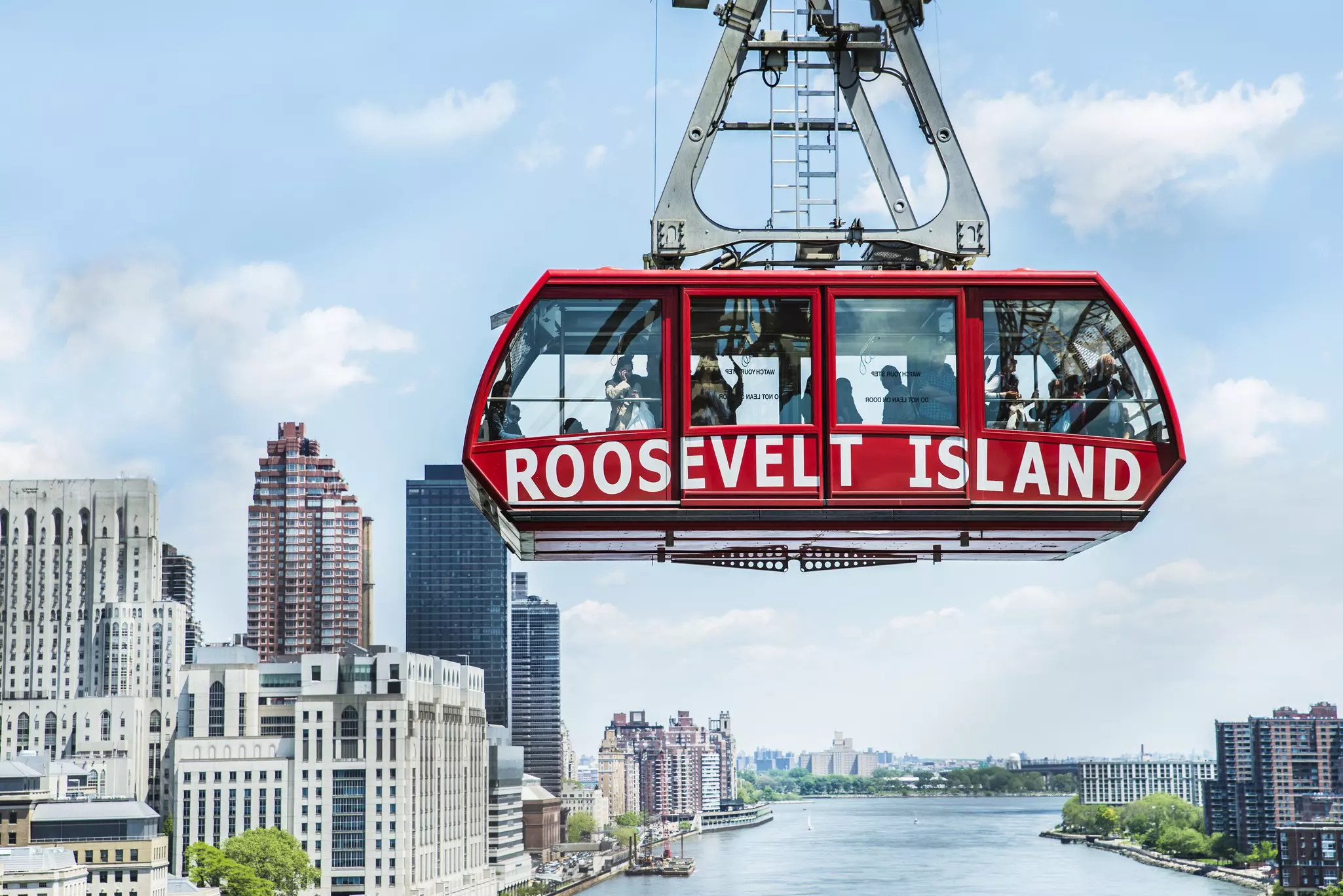 The bright red Roosevelt Island tram suspended over the East River, with Manhattan skyscrapers in the distance