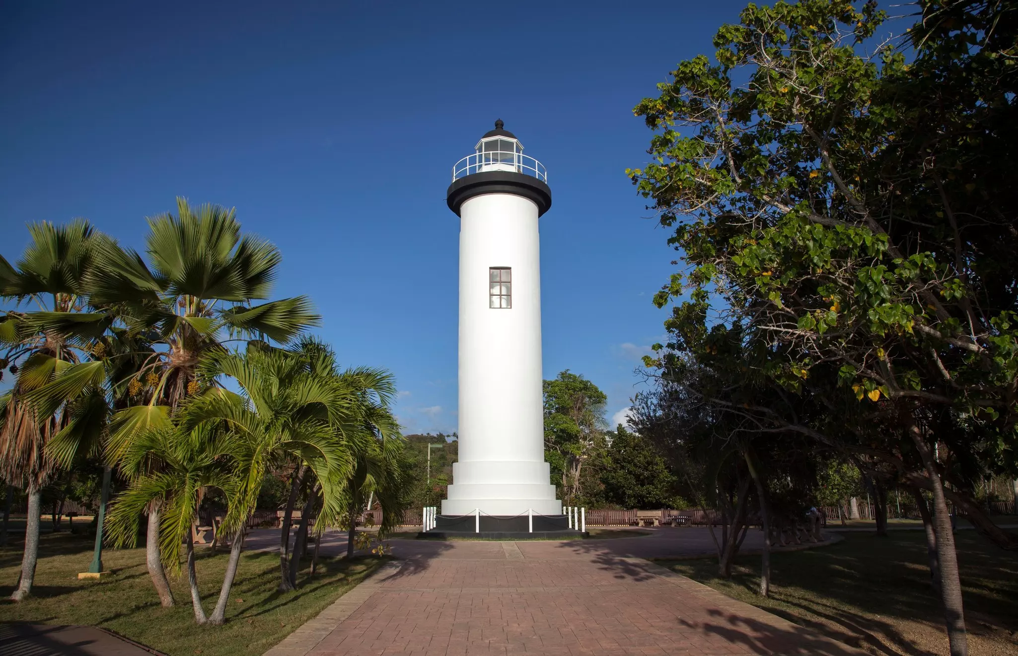 The Punta Higüera Lighthouse under a blue sky with trees all around