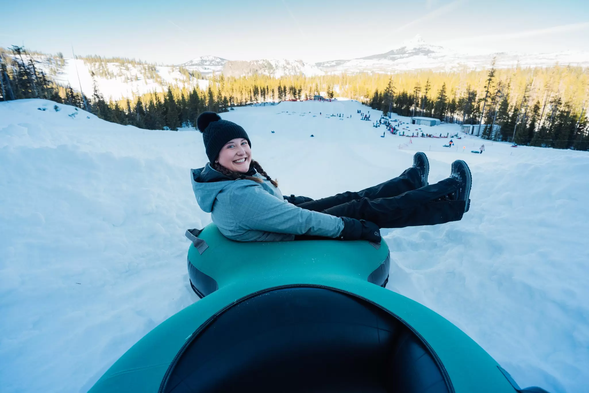 A woman smiles as she sits on a sled going down a snowy slope, Hoodoo Ski Area, Central Oregon