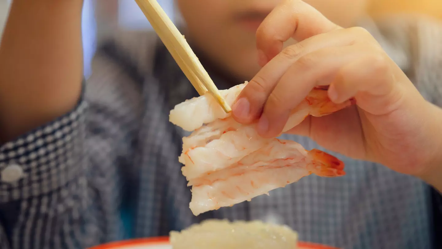 Young boy eating sushi with chopsticks