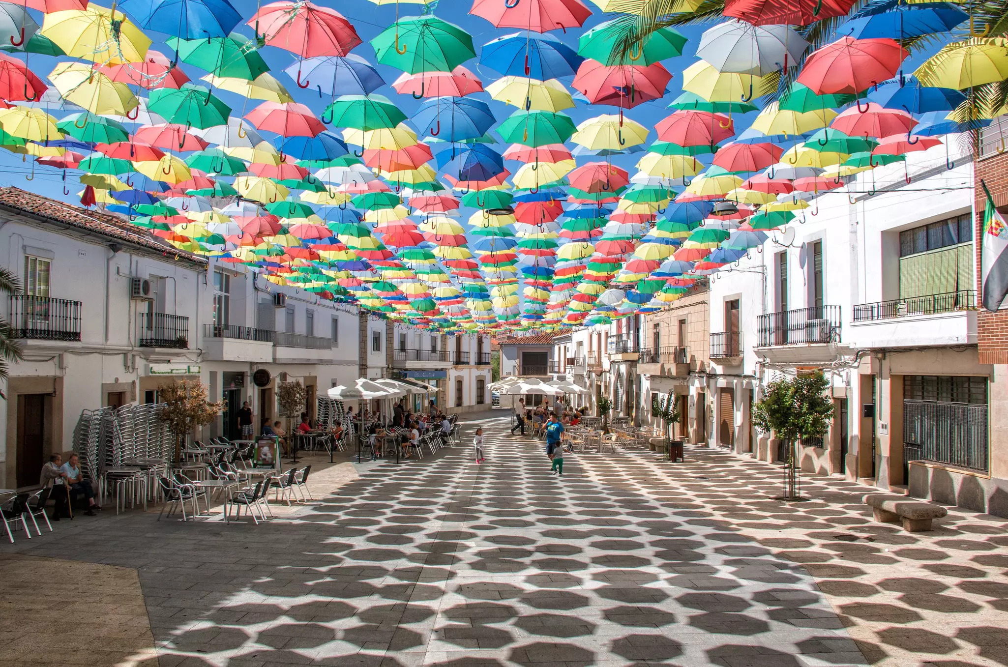 Hundreds of colorful umbrellas hanging above a city square on a sunny day.