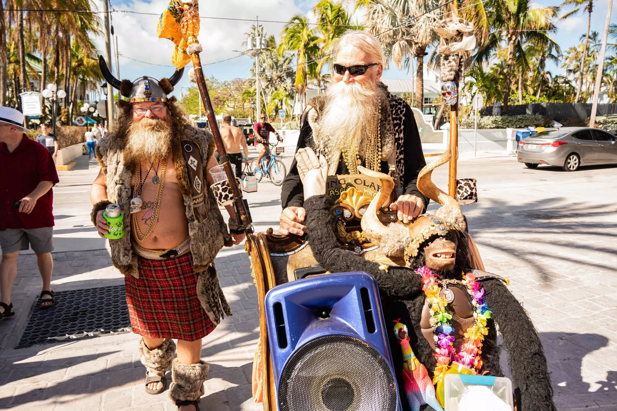 Men with long beards and in costumes walk down the street in a sunny location.