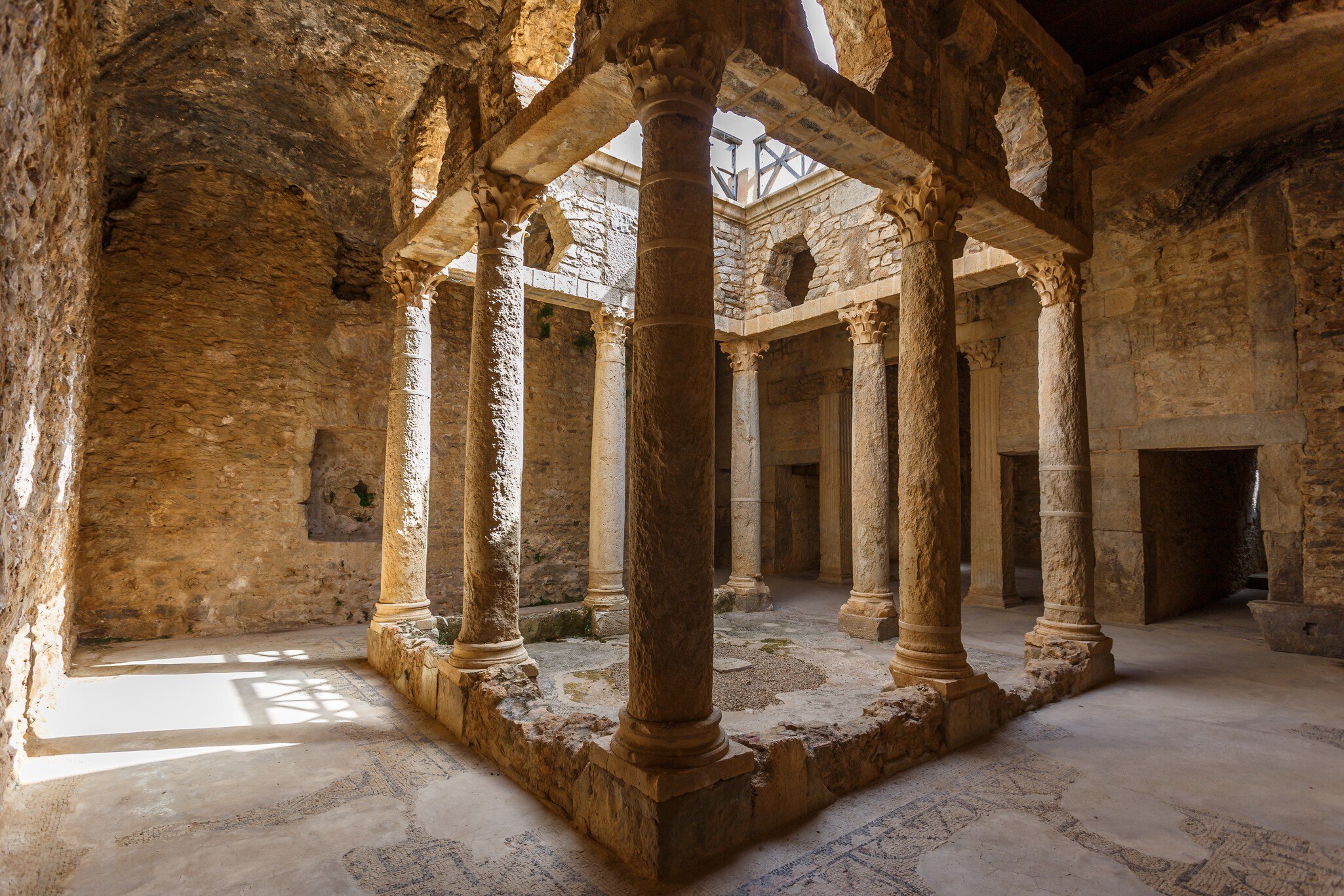 Columns ring a sunlit sunken courtyard, with mosaic floors in the vaulted galleries around it.