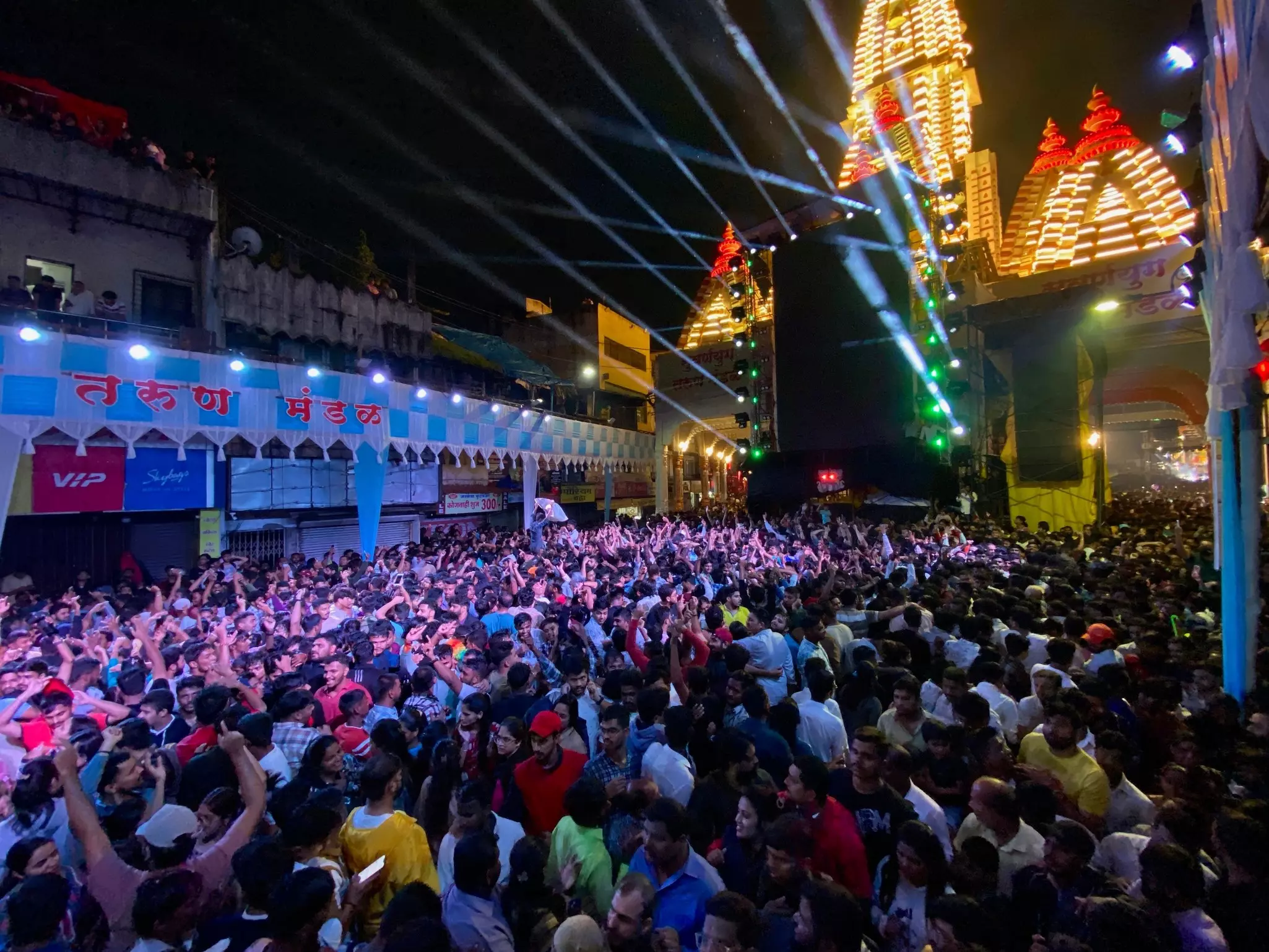 A dense crowd dances to music at an outdoor festival at night, illuminated by stage lights.