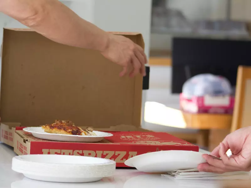 Hands reaching in to pick up slice of pizza from Jet's Pizza