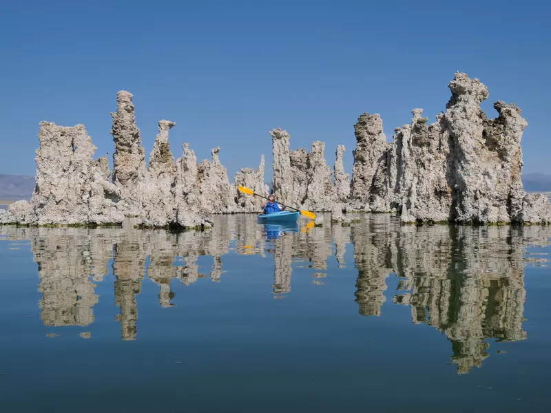 A kayaker with a yellow paddle near tufa formations emerging from a blue lake.