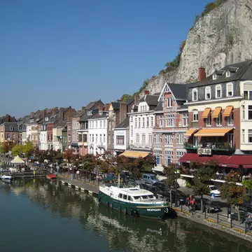 Colorful riverside buildings housing restaurant and bars line the river in Dinant, with boats moored along the waterfront.