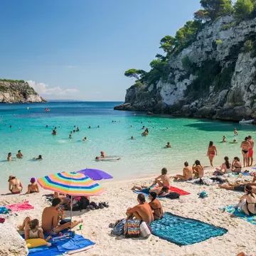 A beach in Menorca, Spain with people sitting on blankets and swimming in the water. 
