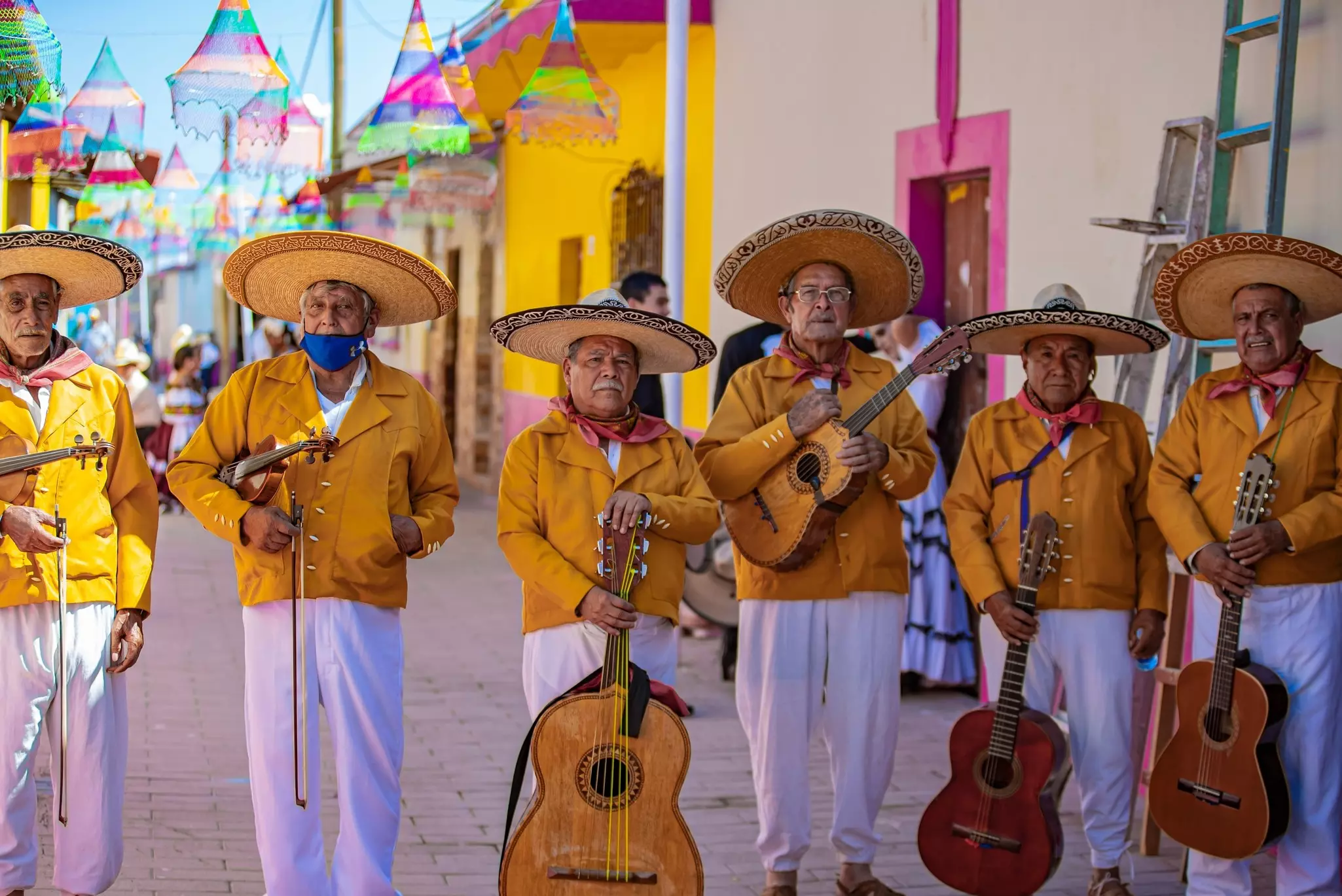 A group of mariachi musicians wearing orange jackets perform in a street.