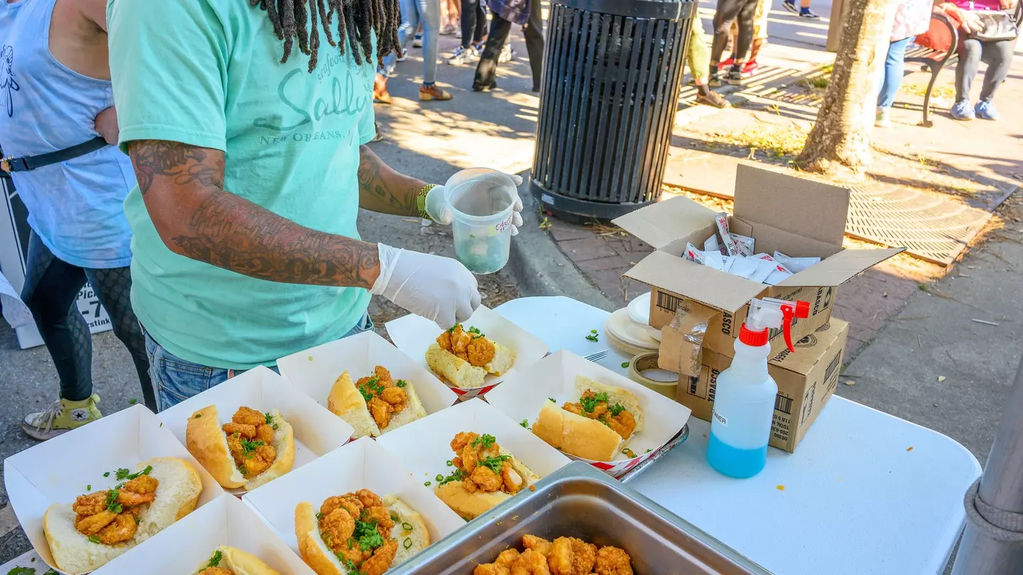 Grilled shrimp is placed on top of onions, tomato and lettuce to create an open-face sandwich. There are french fries under the sandwich and a black plastic fork resting on the red tray.