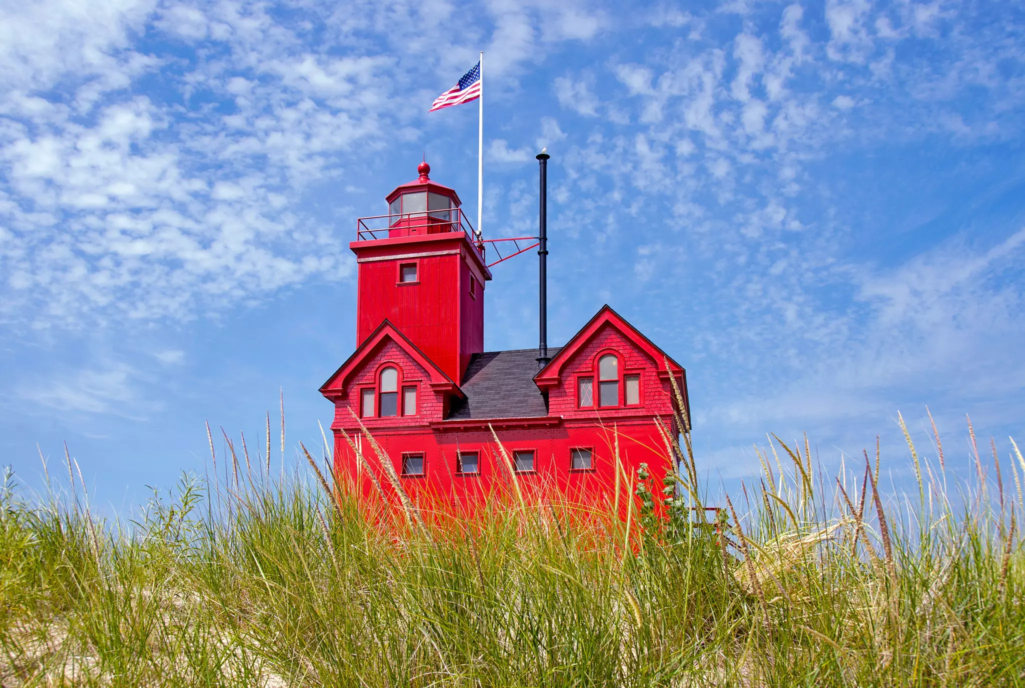 A squat square red lighthouse on a grassy dune.