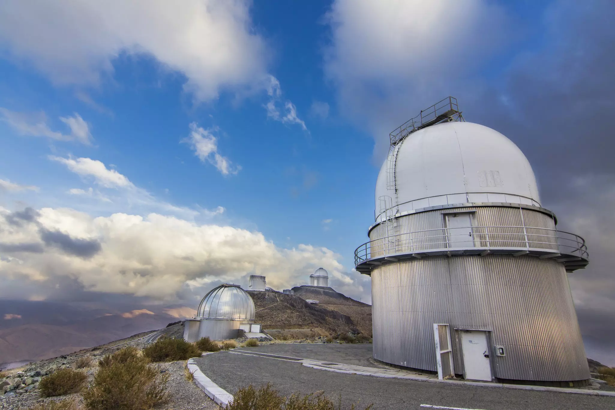 Several domed observatories lining a high ridge in a desert landscape