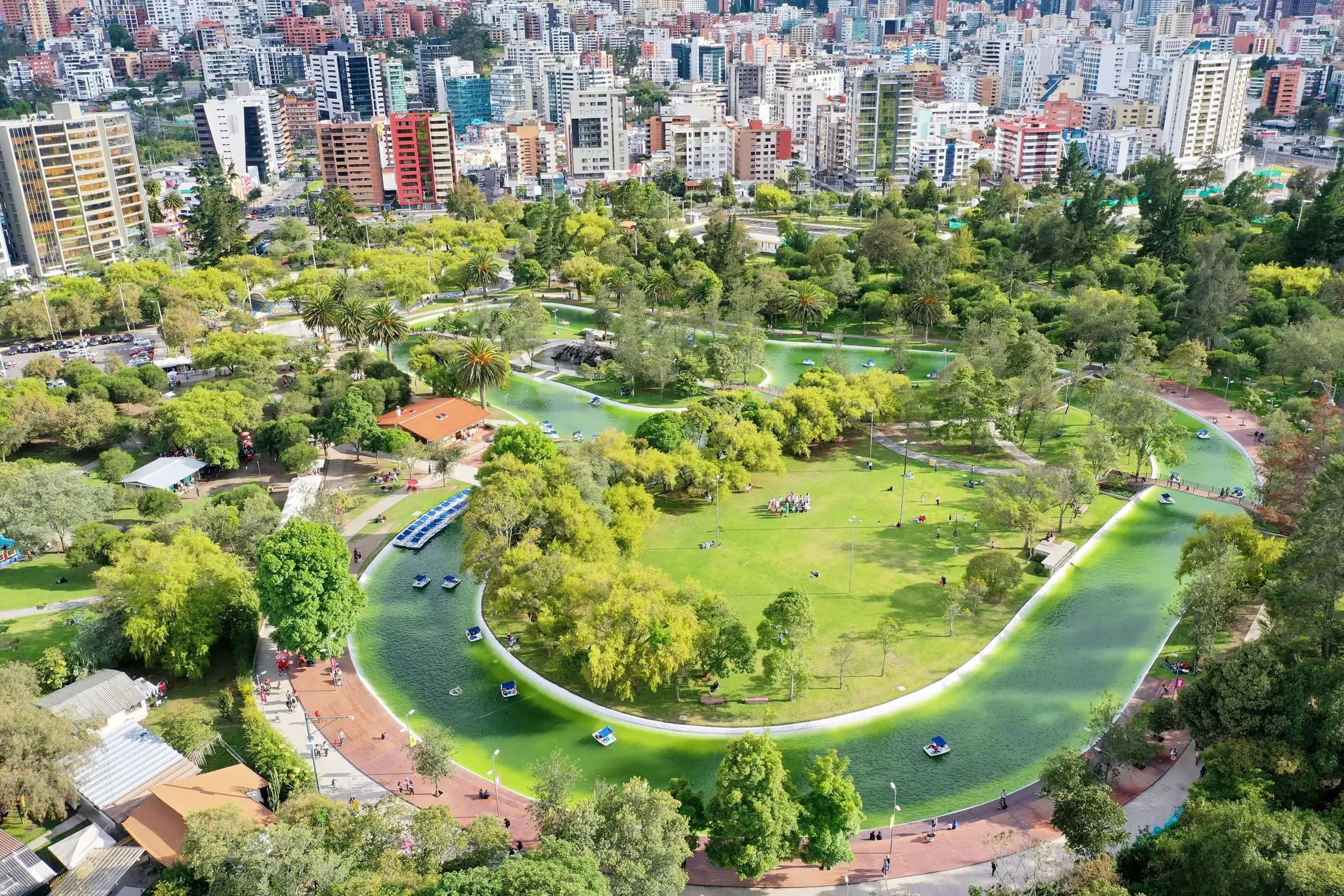 An aerial view of a city park surrounded by tall buildings. A windy lagoon snakes through the park.