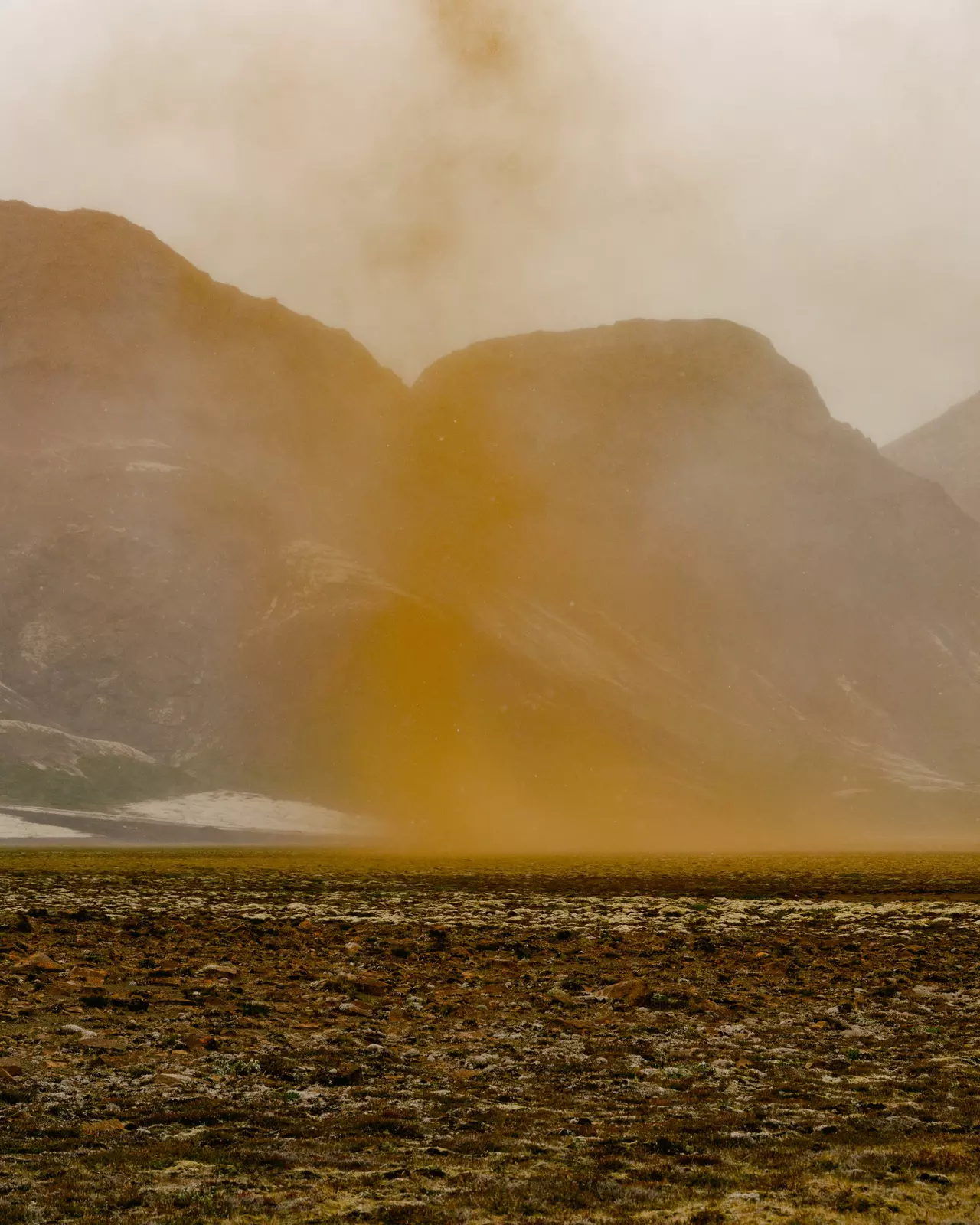 Dust over a landscape with mountains and grey sky in the background 