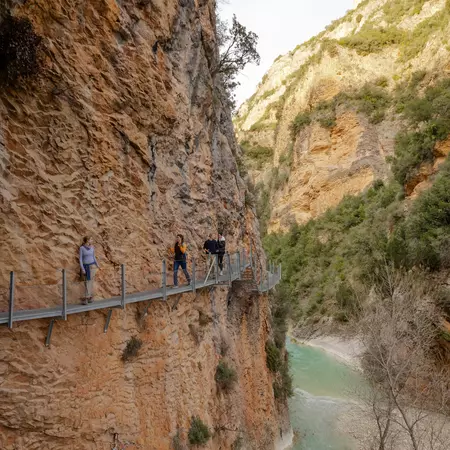 People walk on a narrow walkway on the side of a cliff.