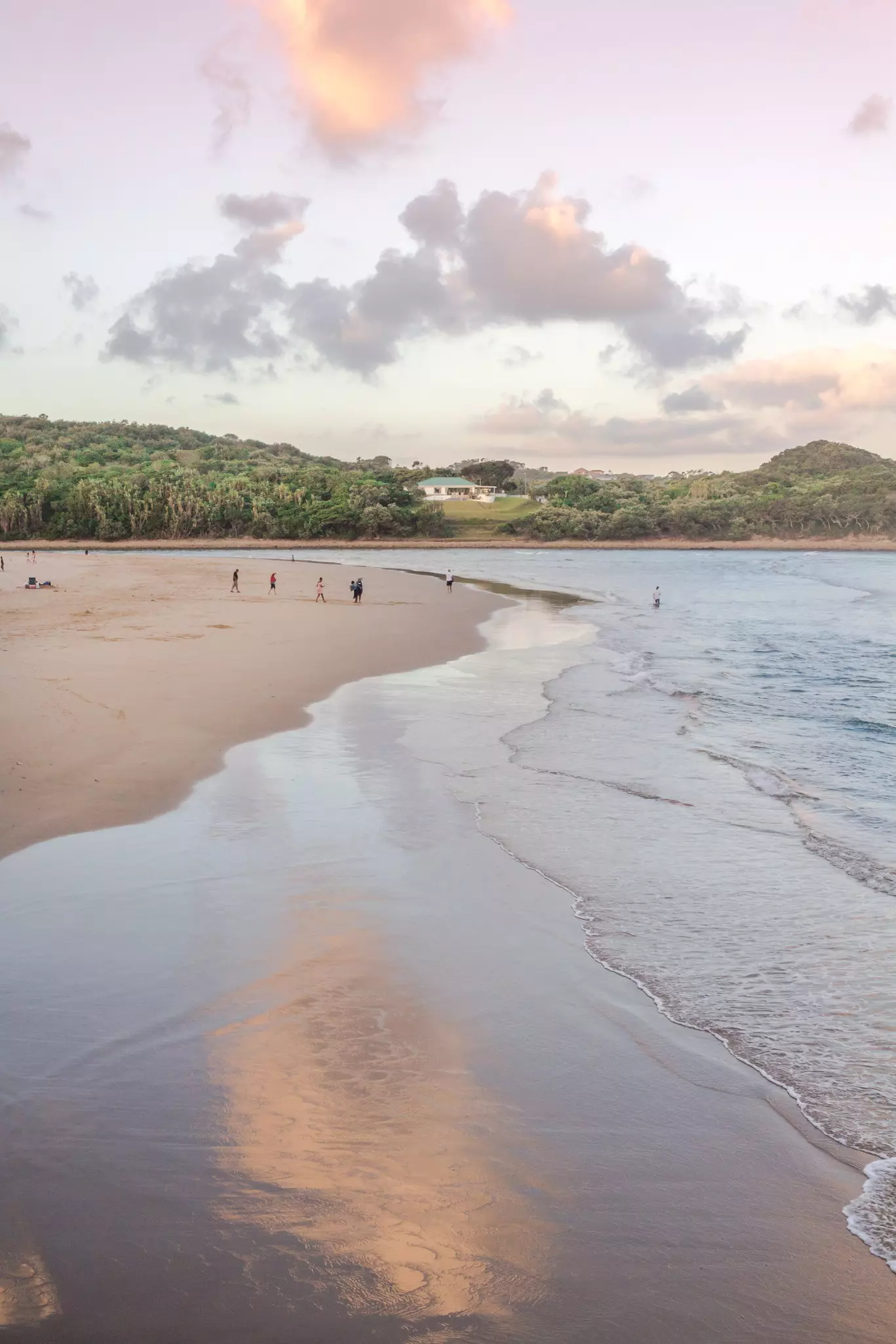 A family walks over the wide sands of a riverside beach towards the water.