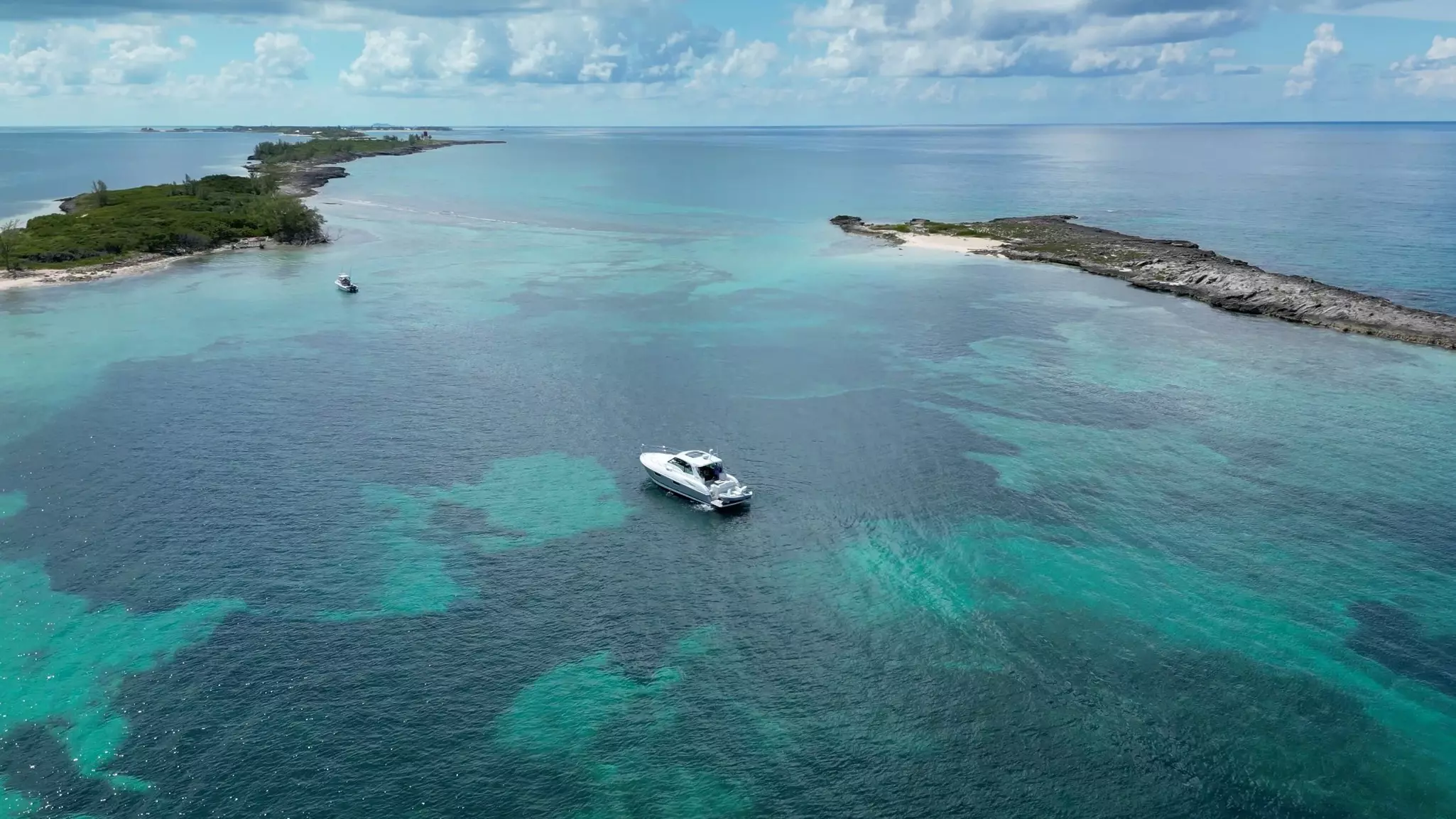 An aerial view of a single boat in the center of a harbor with turquoise water speckled with darker areas.