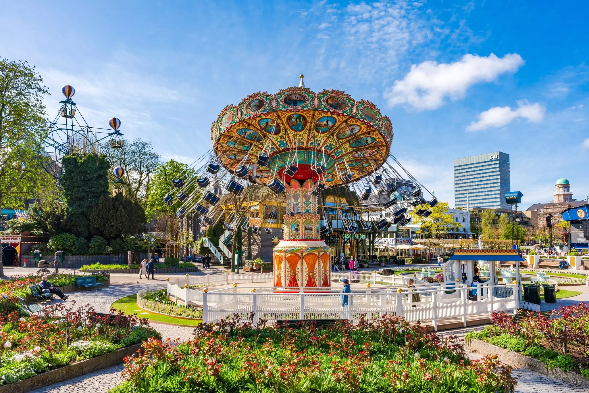 Colorful rides at an amusement park with city buildings in the distance on a sunny day.
