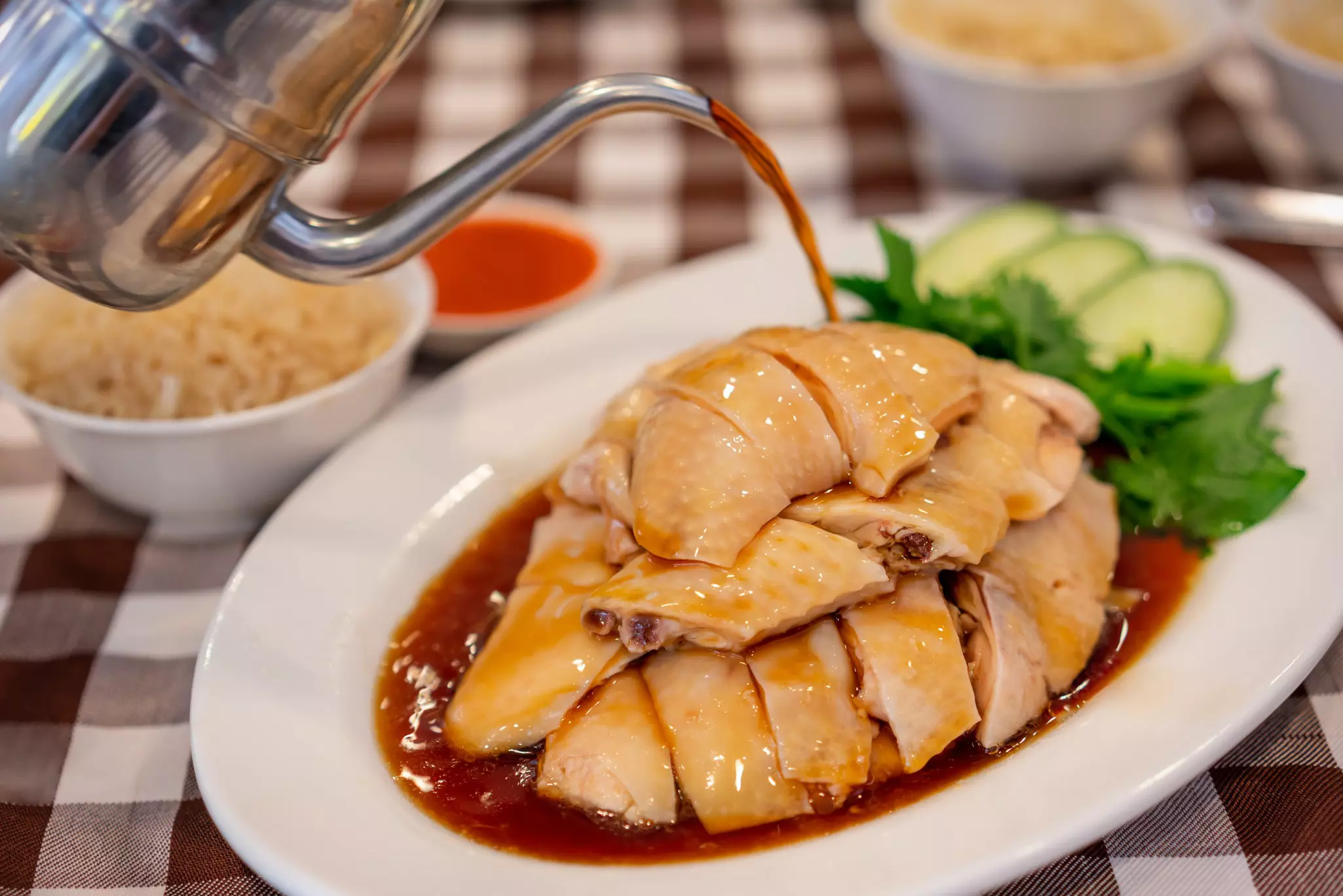 A person pours sauce over a plate of sliced chicken at a restaurant.