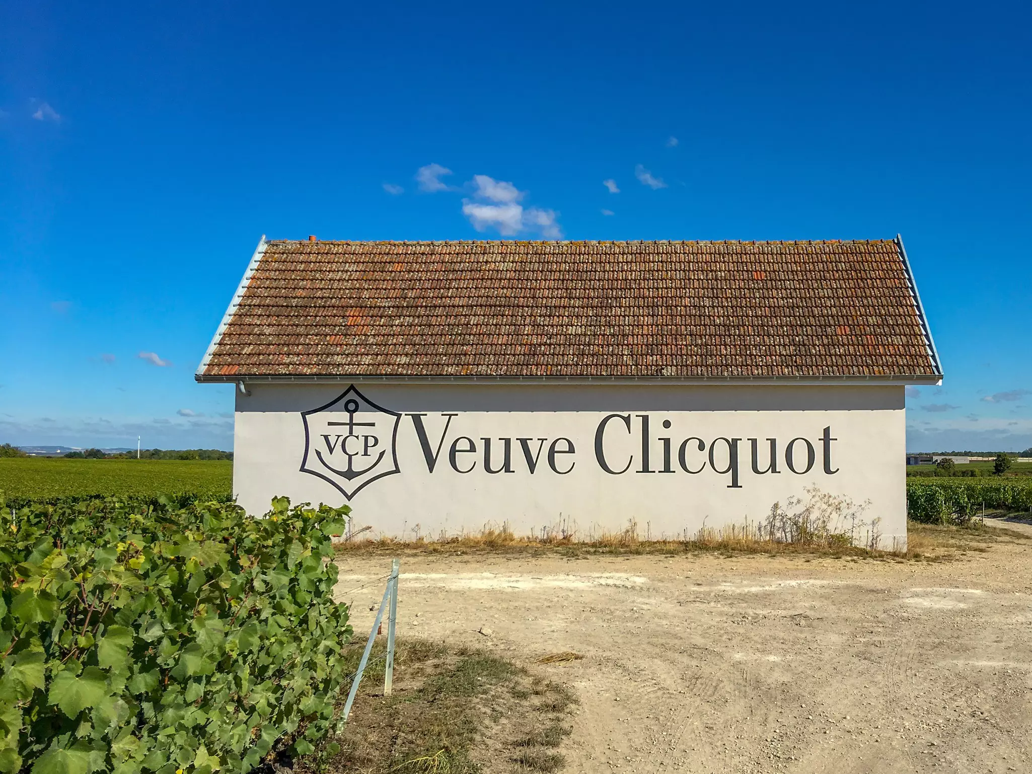 A white building with the words Veuve Clicquot paineted on the side with grape vines to the left.