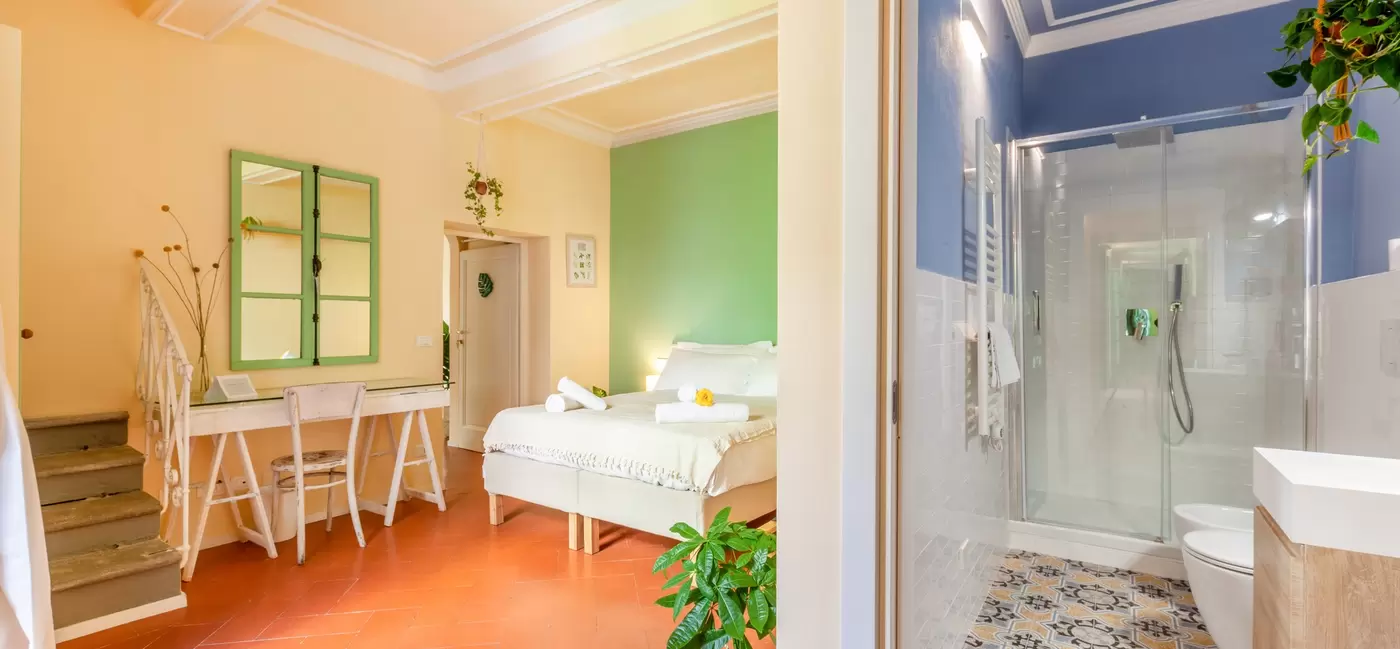 split view of a bedroom with pale-green walls and a it's corresponding bathroom with blue walls and intricate floor tiles