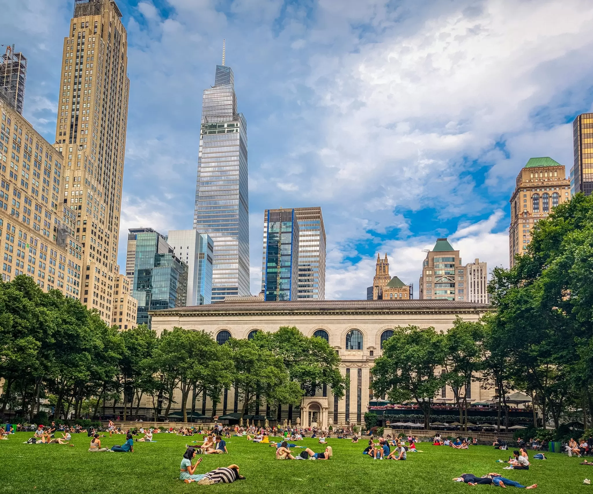 A section of green space among tall skyscrapers. People are relaxing on the grass on a sunny day.