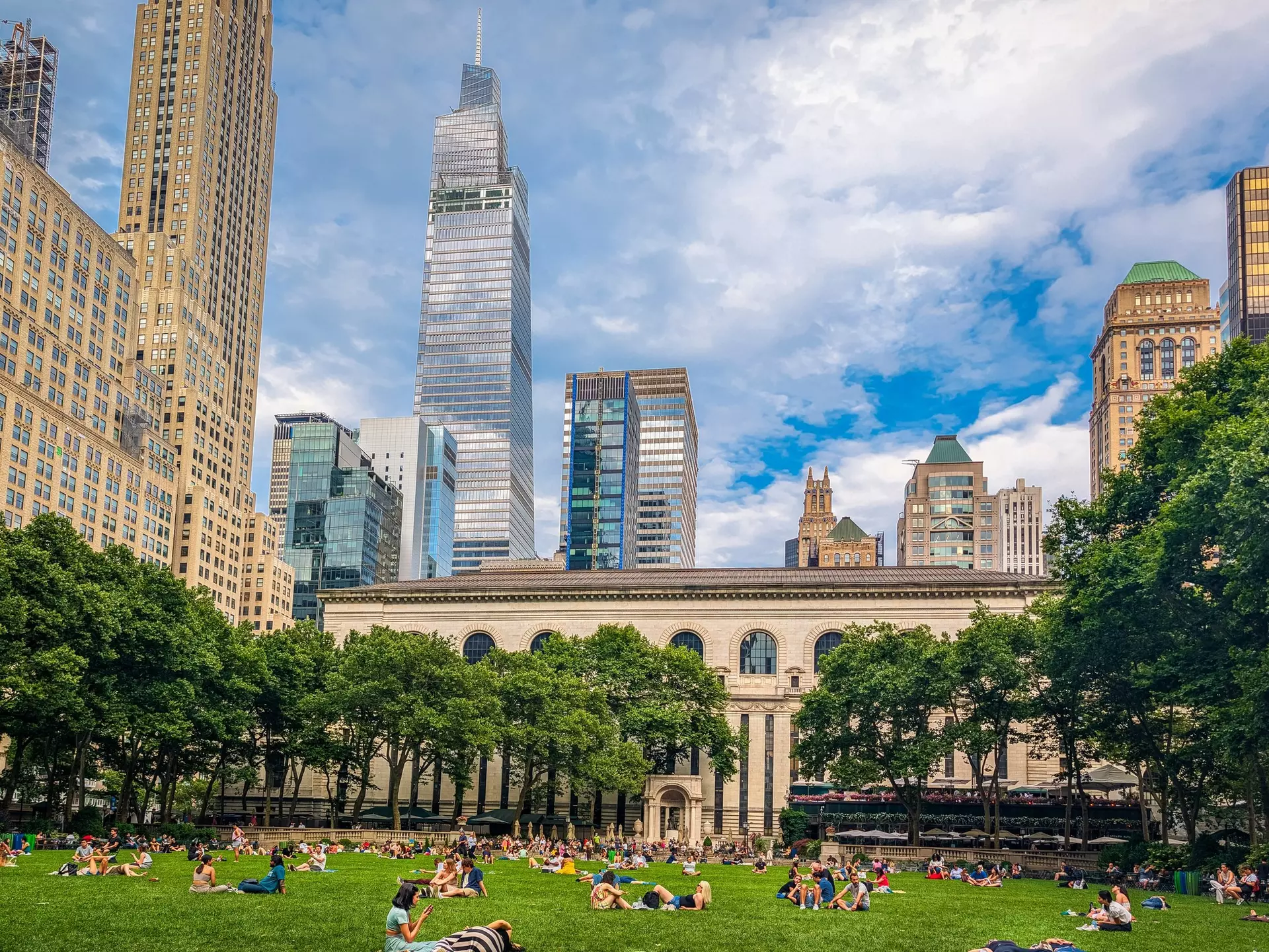 A section of green space among tall skyscrapers. People are relaxing on the grass on a sunny day.