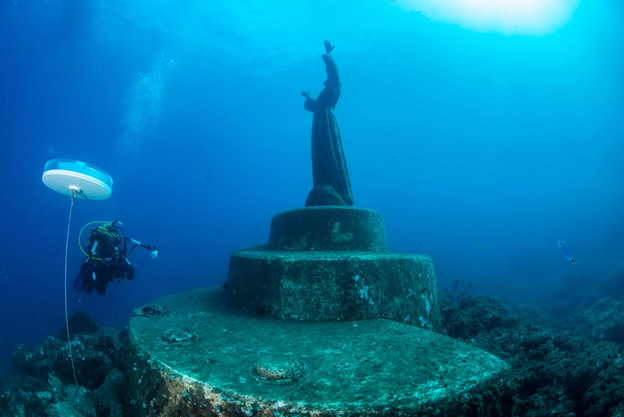 A diver swims near an underwater statue of Christ