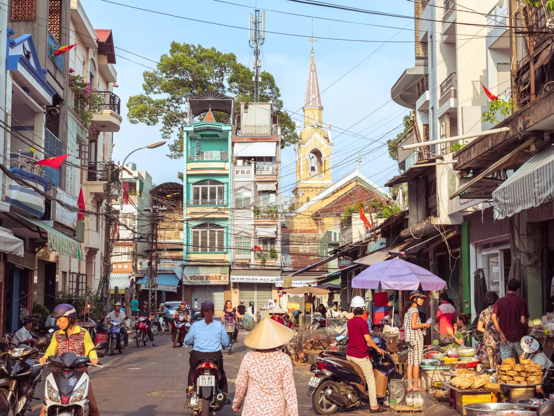A picturesque street of Cholon buzzing with market activity, a view of townhouses and Cha Tam Church (St. Francis Xavier Parish Church).