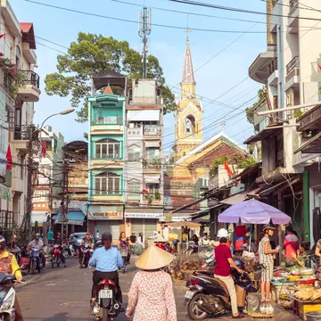 A picturesque street of Cholon buzzing with market activity, a view of townhouses and Cha Tam Church (St. Francis Xavier Parish Church).