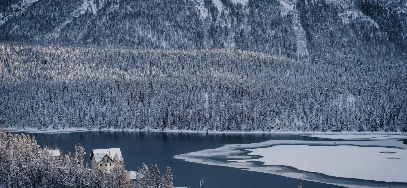 A partially frozen lake with snowy trees around the perimeter.