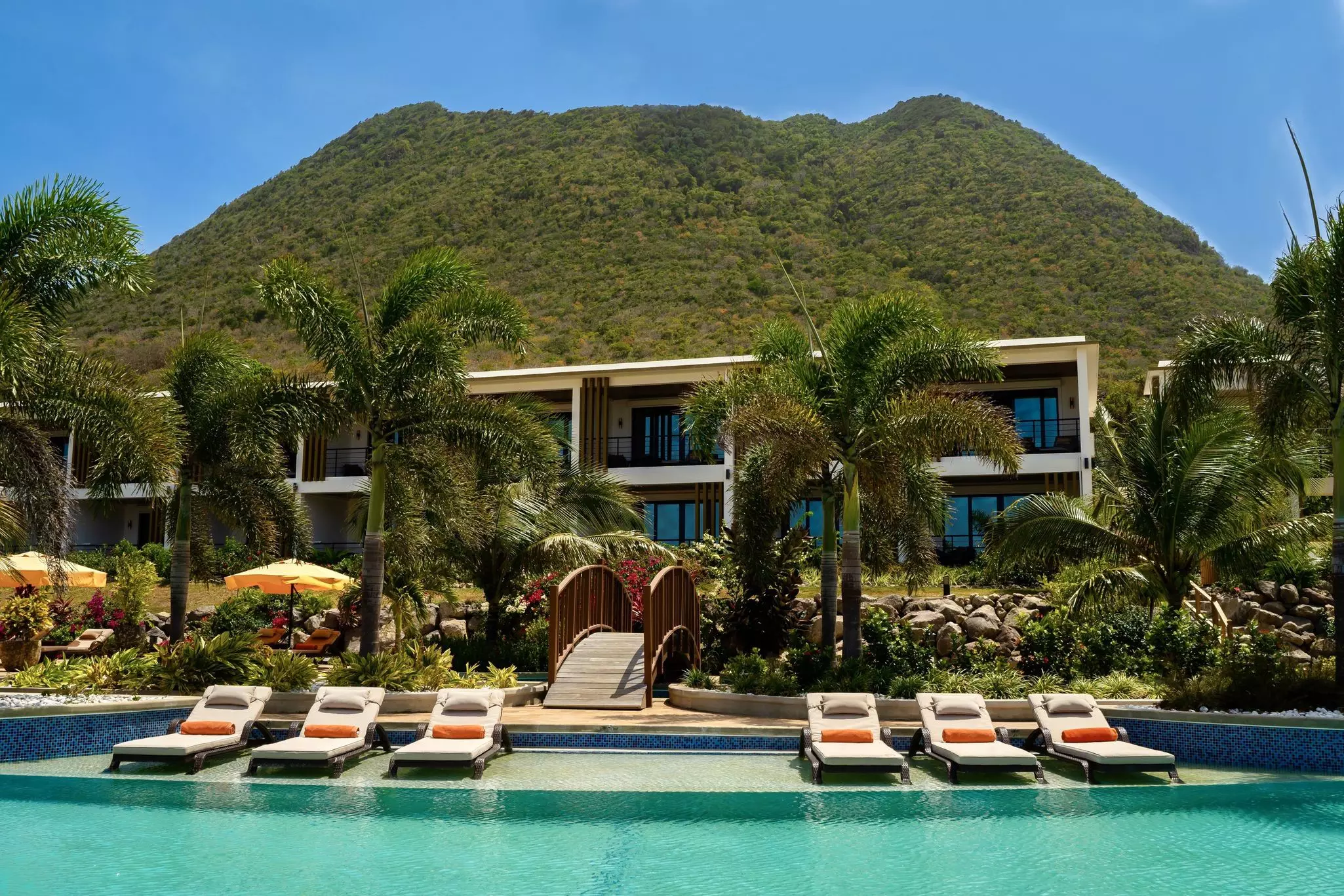 A group of chairs are lined up in front of a pool at Golden Rock Resort. In the background, there's a wooden bridge
