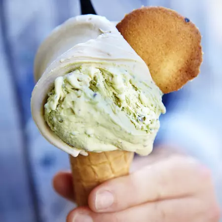 A person holds a pistachio and hazlenut gelato ice cream cone.