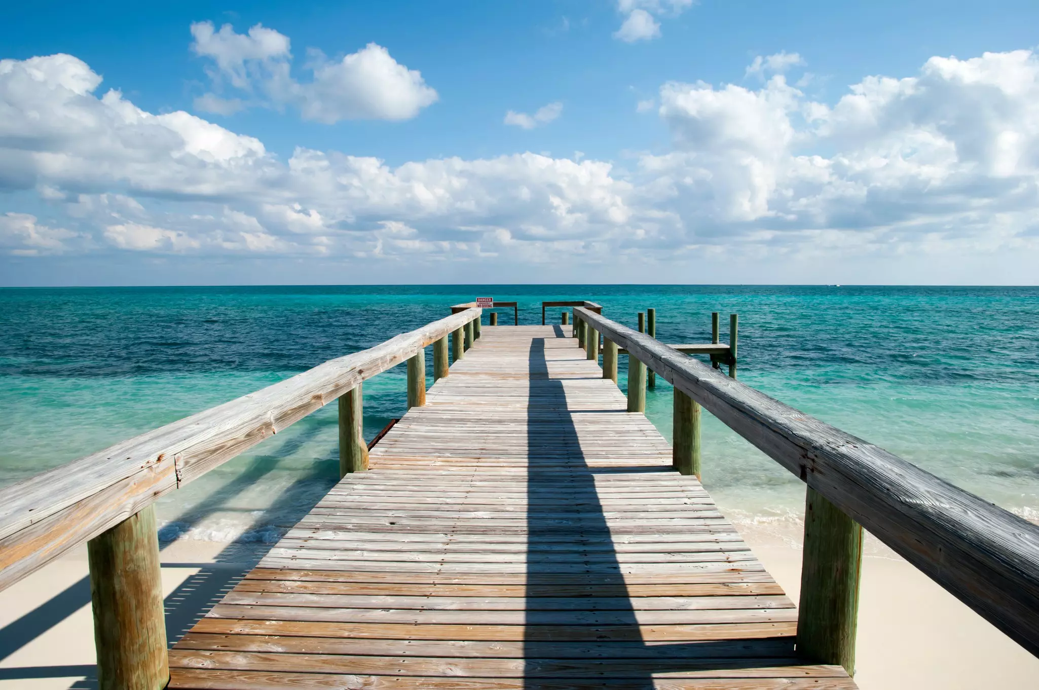 The view of Caribbean Sea and the wooden pier with a warning sign on Taino Beach, Grand Bahama Island.