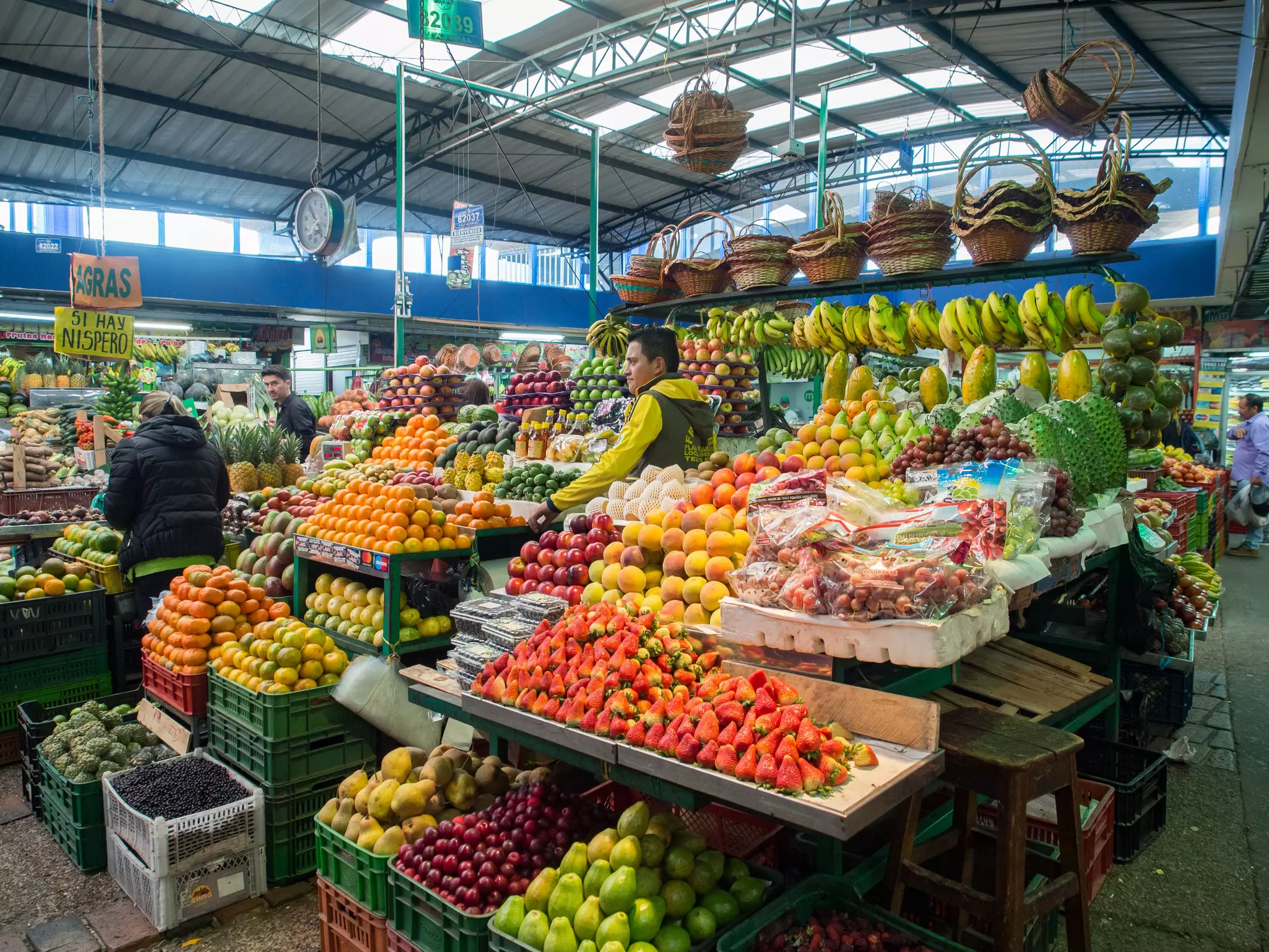Market stalls are piled high with colorful fruits at a covered produce market.