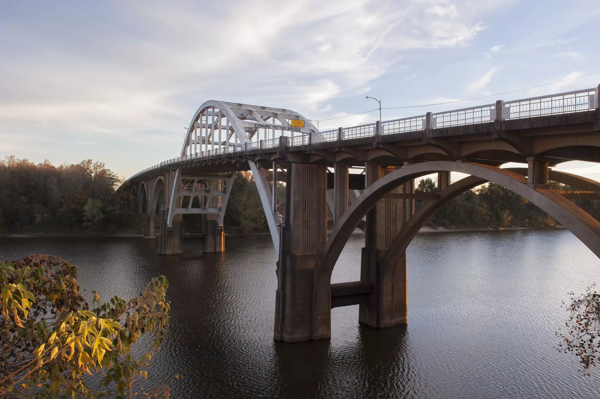 A stone bridge with curved trusses over a river at sunset.
