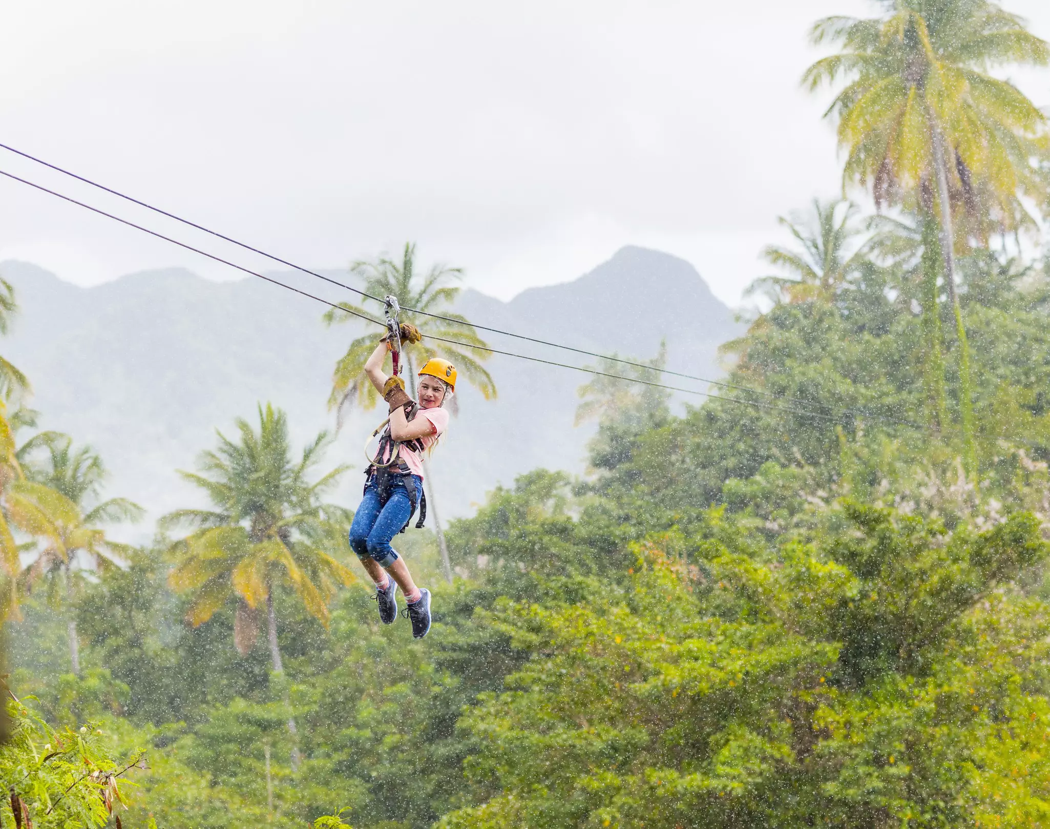 A woman ziplines over a jungle canopy in St Lucia in the rain.