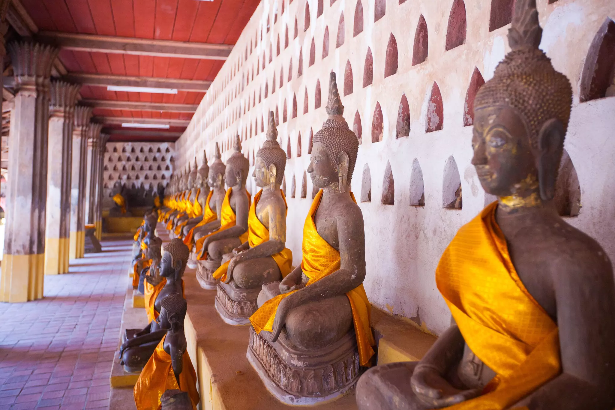 A row of seated Buddha statues lined up in front of a wall. 