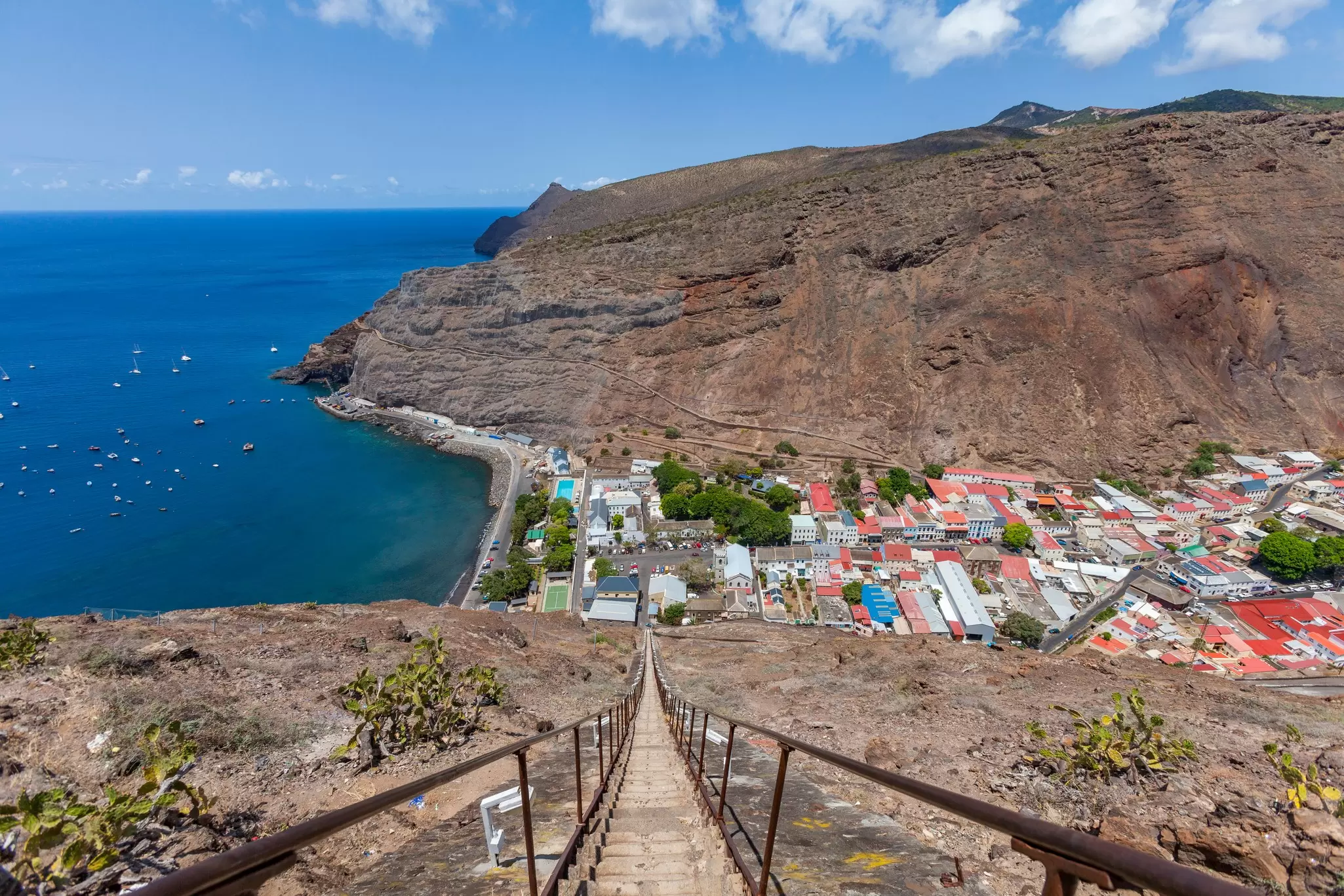 A steep staircase on a rocky hillside leads to a town in a dry valley.