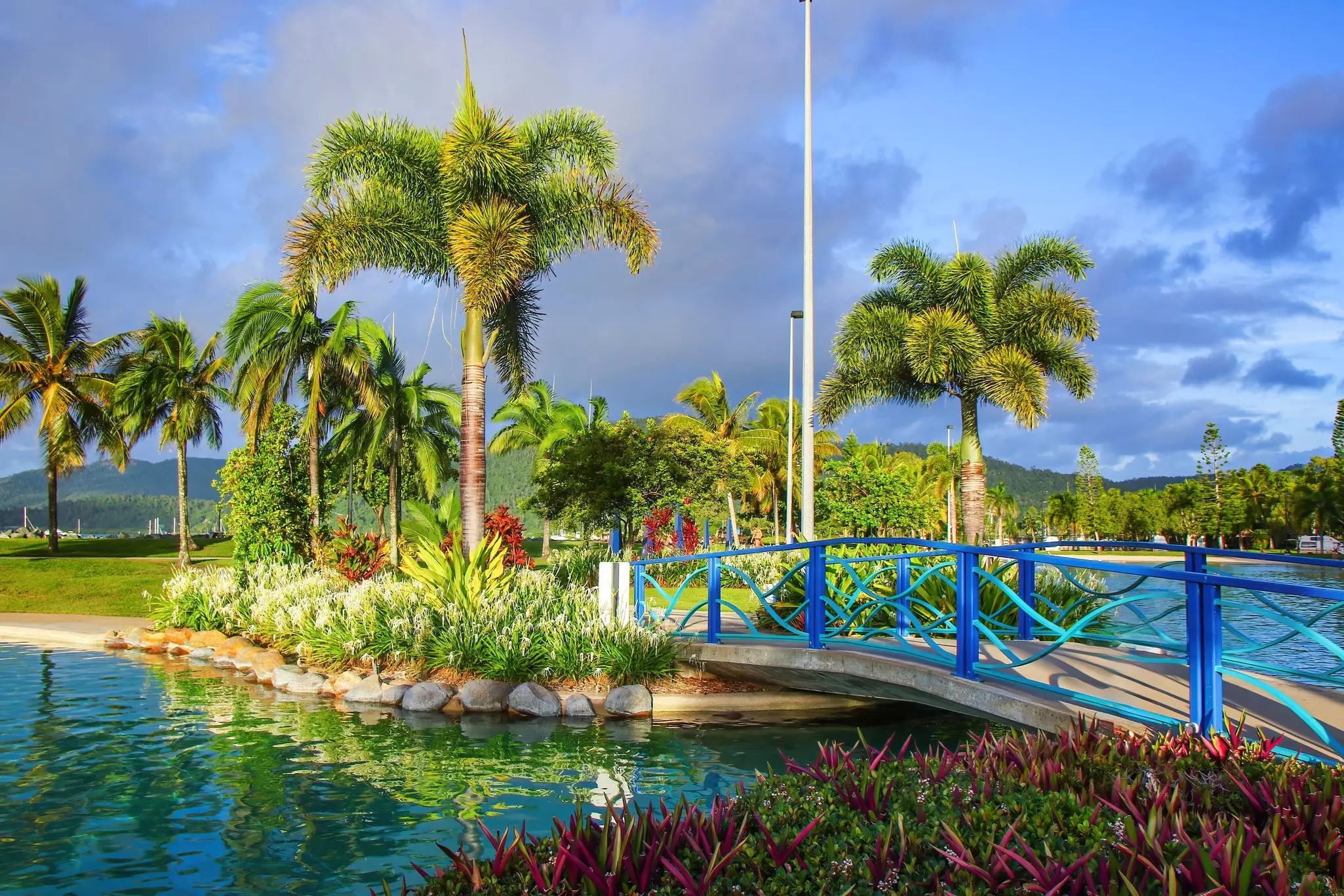 A bridge with blue railings crosses a lagoon in Australia's Whitsunday Islands; there are lush landscaped plantings on either side.