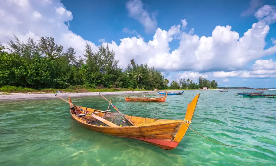 Pulau Bintan: wooden fishing boat with nets moored in clear turquoise shallows off a sandy, tree-lined beach