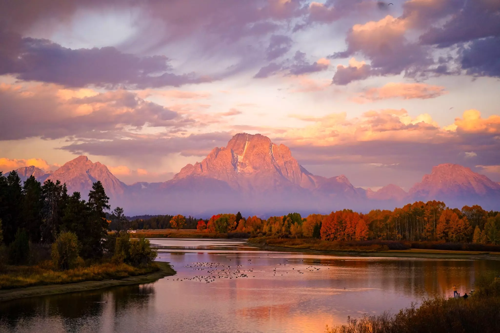 A mountain towers over a river glinting pink in the light