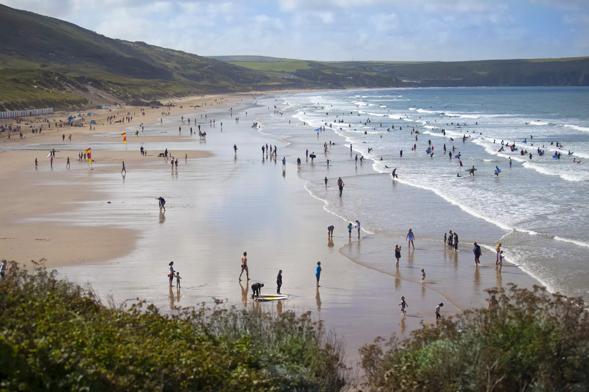 Surfers head out into the waves off the shores of a wide stretch of golden sandy beach