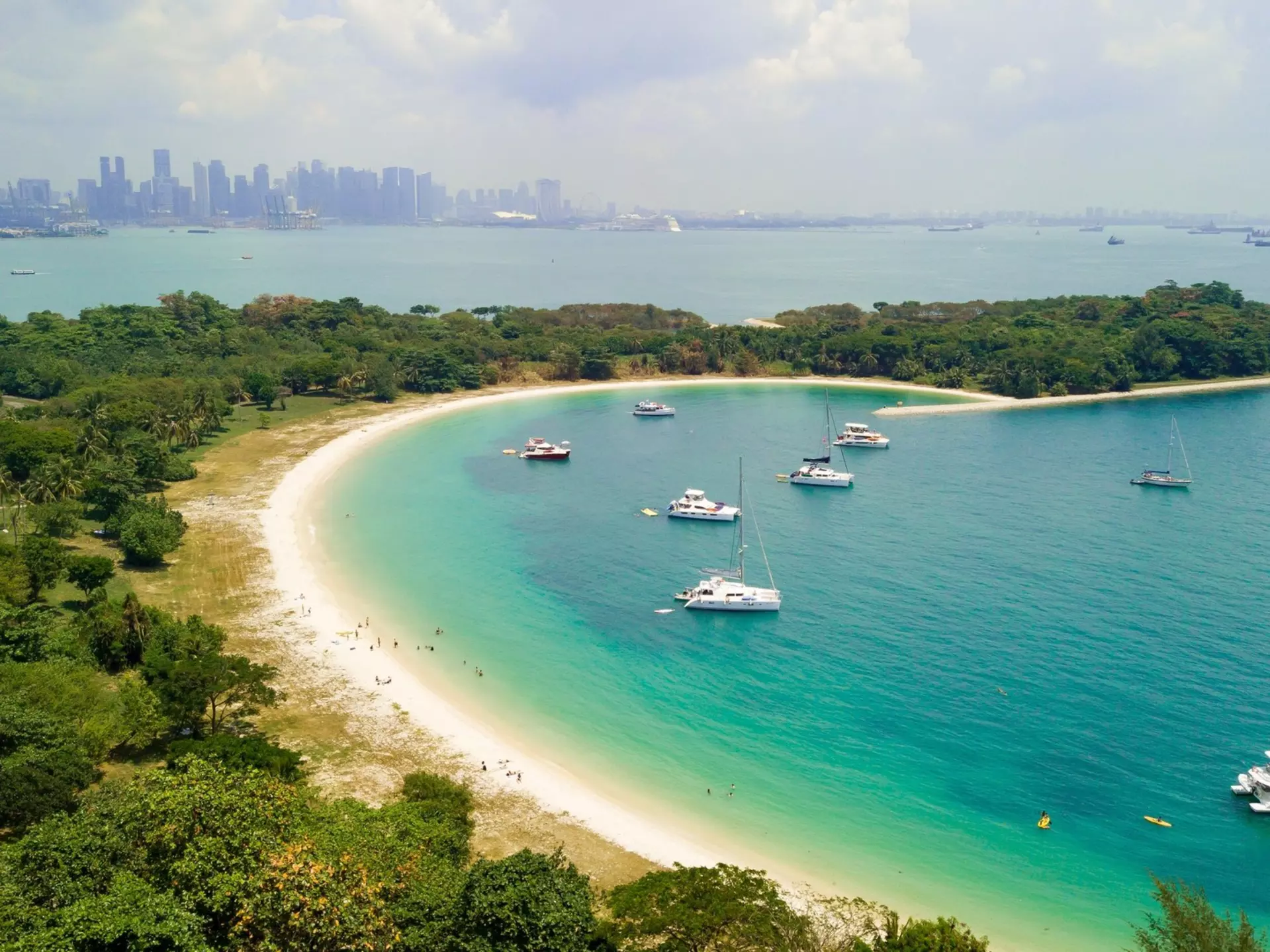 Aerial picture of the beach of Lazarus Island with yachts moored in the cove and the city visible in the distance, Singapore