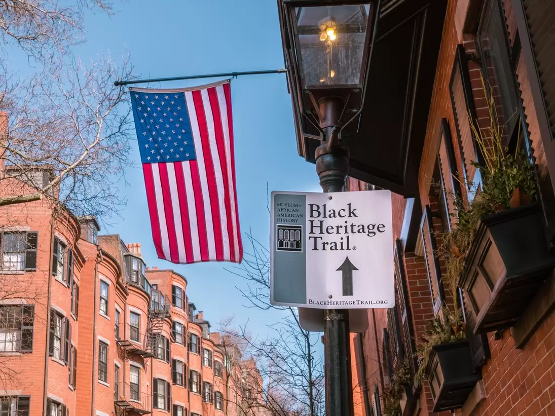 Boston, MA, US-June 10, 2023: Black Heritage Trail sign in Boston's historic Beacon Hill nieghborhood with American flag and 19th century brick buildings in background., License Type: media, Download Time: 2024-09-10T06:43:40.000Z, User: oneseven7891, Editorial: true, purchase_order: 56530, job: Global Publishing WIP, client: Pocket Boston 6, other: Dominic Allen